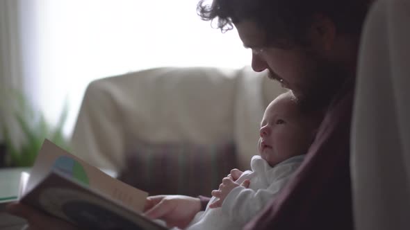 Father with newborn baby reading book at home