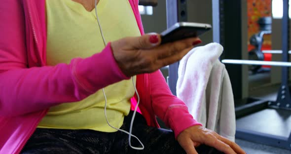 Senior woman listening music on mobile phone in fitness studio