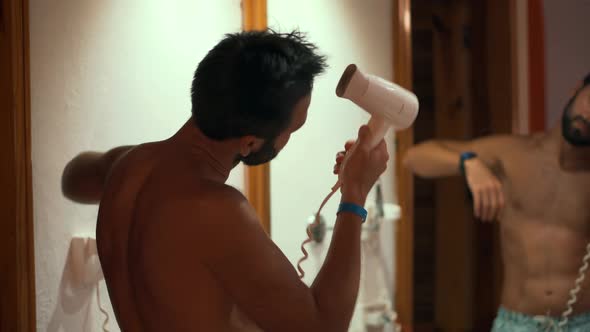 Man Dries Hair In Hotel Room And Finish Hairdressing. Man Drying His Hair In Bathroom From Mirror