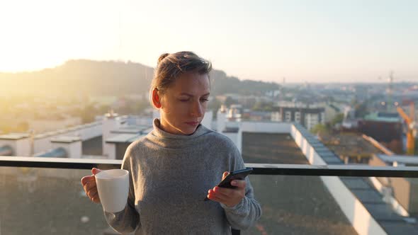 Woman Starts Her Day with a Cup of Tea or Coffee and Checking Emails in Her Smartphone on the