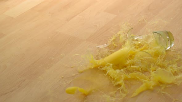 Dropping Glass of orange juice and breaking on wooden floor, Slow Motion