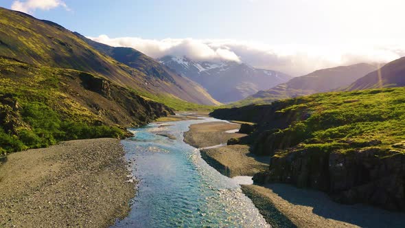 Flying Above a Glacial River in Iceland with Snowy Mountains in the Background