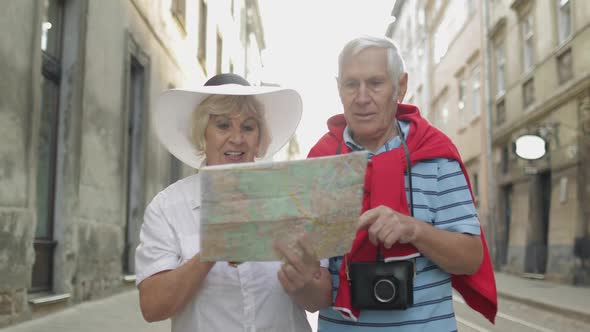 Senior Male and Female Tourists Walking with a Map in Hands Looking for Route