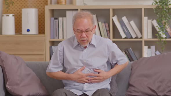 Senior men holding his stomach feeling pain while sitting on the sofa at home. Asian man having stom