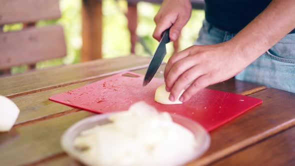 Close-up: The Guy Is Cooking Pilaf. He Is in a Summer House, Cuts Onions, on a Red Cutting Board