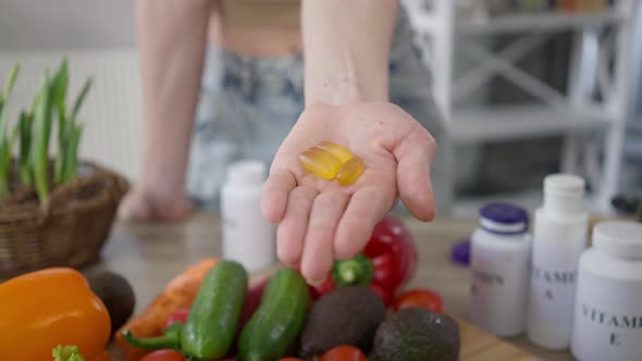 Closeup Female Fist Opening Palm with Yellow Vitamins at Table with Healthy Vegetables