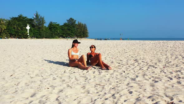 Pretty happy ladies on photoshoot by the sea on beach on sunny blue and white sand background 