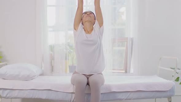 Calm of wellness Asian young woman sit on bed breathing and stretching before do yoga