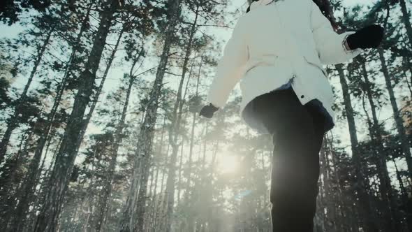 A Young Woman Runs Among Tall Pines Against the Background of Sunbeams in the Winter Forest