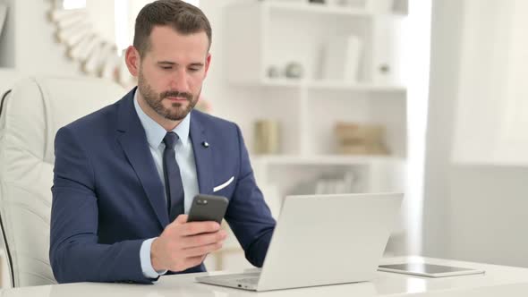 Professional Businessman Using Smartphone and Laptop in Office