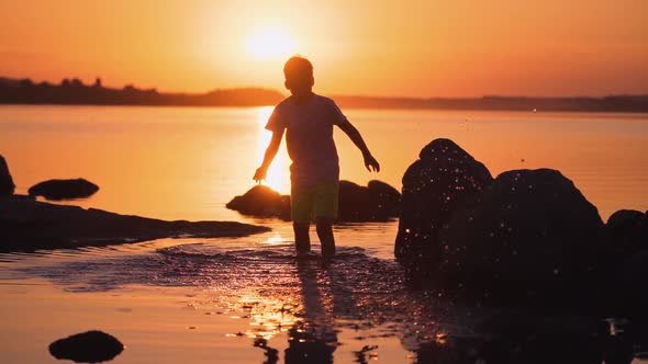 Boy walking in water at sunset. Silhouette of a child in clothes standing inside the river