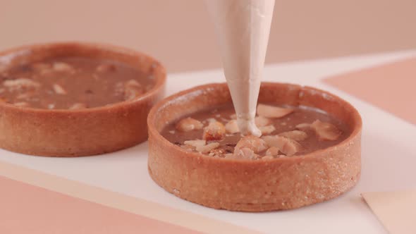 The Pastry Chef Fills a Nut Tart with Mousse on a Beige Background