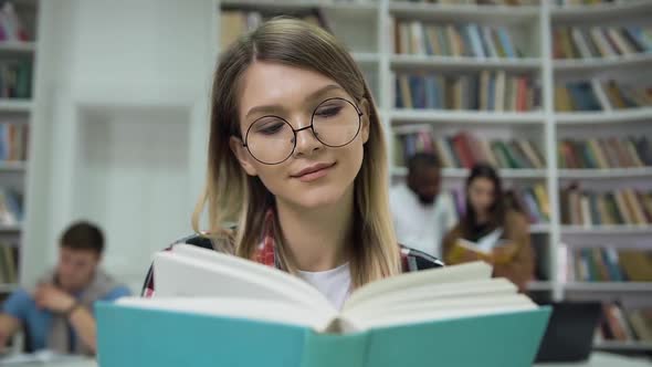 Pretty Calm Concentrated Young Woman in Glasses Reading Book in the University Library