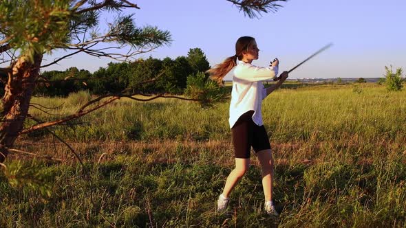 Swords Training  Young Woman Waving with a Sword on Nature at Early Evening on Nature