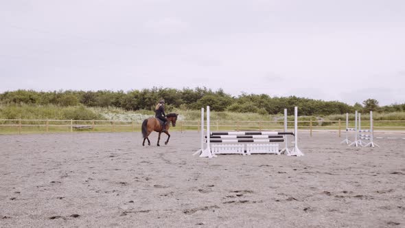 Woman Riding Horse Around Paddock With Jumping Fences