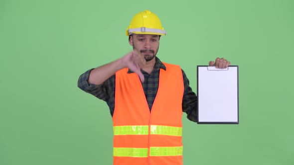 Stressed Young Bearded Persian Man Construction Worker Showing Clipboard and Giving Thumbs Down