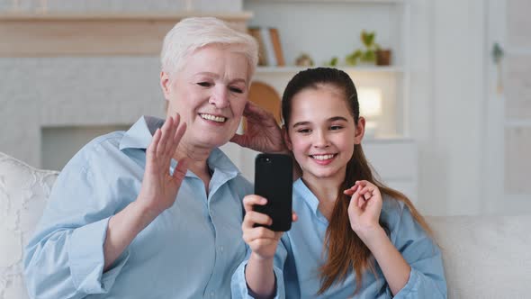 Old Grandmother and Little Granddaughter Having Fun Using Smartphone Look at Screen Laugh Talk Make