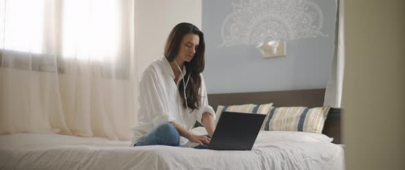 A young woman speaking to someone through earphones while working on her laptop