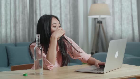 Asian Woman Drinking Vodka While Typing On A Laptop At Home