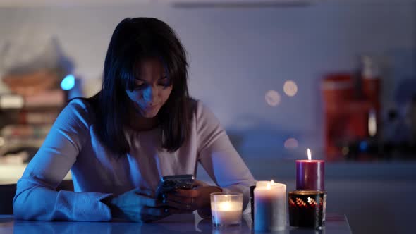 A Darkhaired Thoughtful Woman Sits at a Table and Holds a Mobile Phone in Her Hands in Front of Her