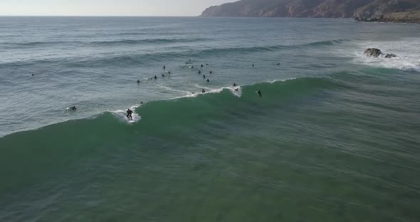 Aerial, reverse, drone shot of surfers waiting for waves,one riding a wave, on a sunny evening, Casc