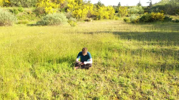 Teenage boy sitting in grass and looking at his smart phone. Camera slowly gliding over him