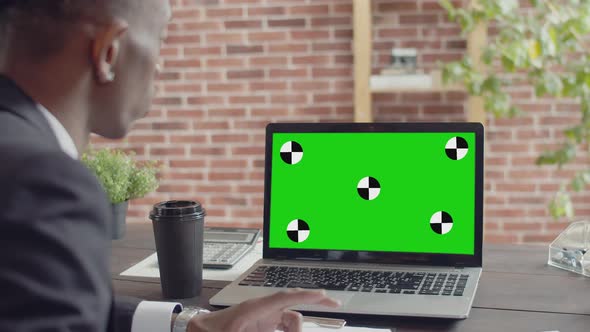 Black Man Businessman in a Suit Speaks By Video Link on a Laptop Sitting at an Office Table with