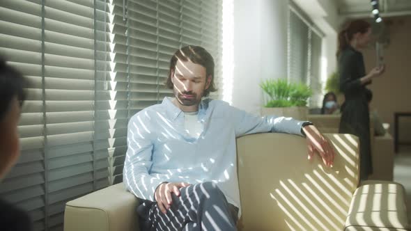 A Young Businessman is Sitting on the Sofa and Talking to His Colleague