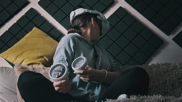 Young Woman in Virtual Reality Helmet Sitting on Sofa and Move Hands at Home