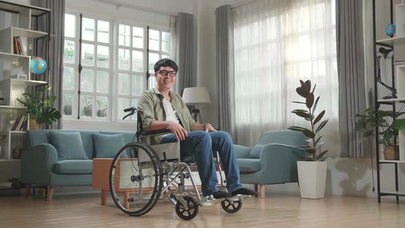 Asian Man Sitting In A Wheelchair Smiling And Looking At Camera In Living Room
