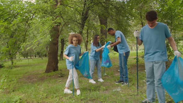 Charming Girl Helping Handsome Young Man to Open Garbage Bag Outdoors