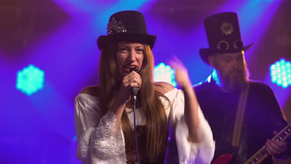 Young Woman Soloist Sings Into Microphone While Standing on Stage with Musical Group