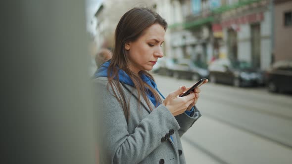 Woman in a Coat Standing on the Street and Using Smartphone