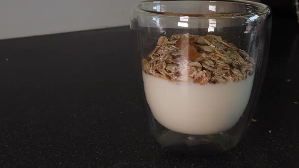 Pouring Raisins ontop of Muesli that was poured optop of Yogurt Into a Class cup (Slowmotion)