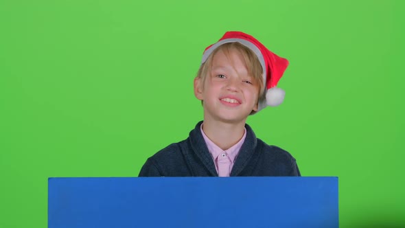 Child Boy Peering Out From Behind Blue Poster Waves a Hand in Front on a Green Screen