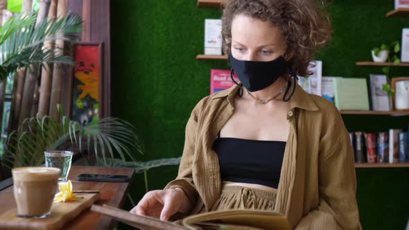 Caucasian Girl in a Protective Face Mask Reading Menu in a Coffee Place