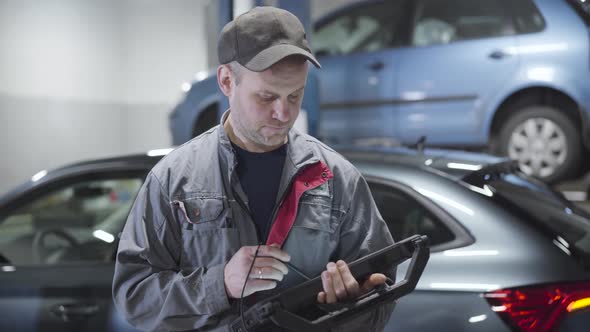 Portrait of Adult Caucasian Man Using Computer and Looking Around in Auto Repair Shop. Professional