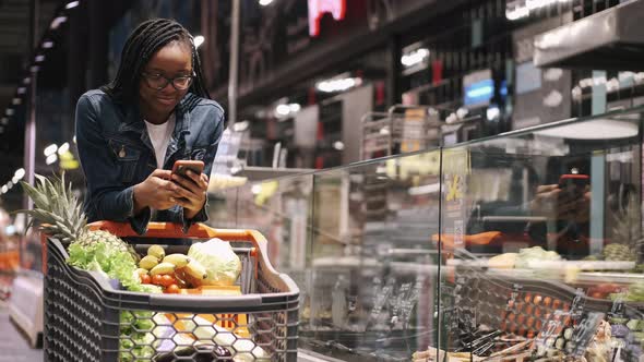 African Amercan Girl with Phone and Trolley in a Supermarket