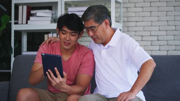 Happy young and senior man using tablet while sitting together on a sofa in a living room.