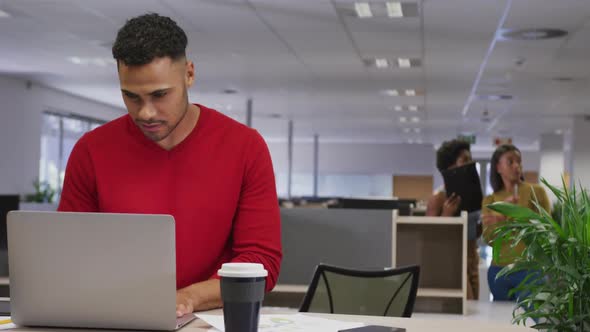 Biracial businessman using laptop over business colleagues in office