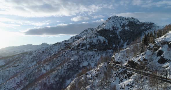 Backward Aerial Top View Over Car Travelling on Road in Winter Snow Mountain Near Forest Woods