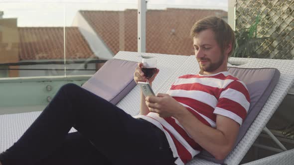 Portrait of relaxing man holding wine glass and using smartphone at a rooftop