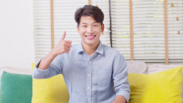 Asian handsome man looking at camera smile and showing thumbs up at home