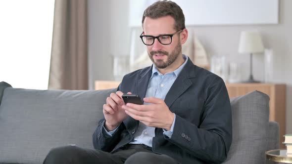 Young Businessman Celebrating Success on Smartphone at Home