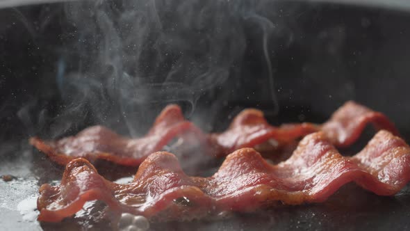 Camera follows cooking bacon on grill. Slow Motion.