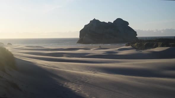 The wind is carrying sand over sand dunes in front of the archway islands at Wharariki Beach, New Ze