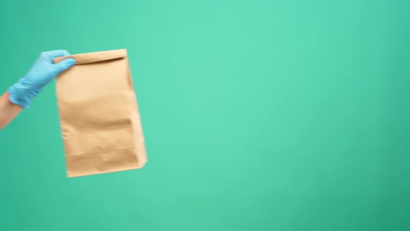 Courier in Gloves Passing Craft Shopping Bag with Delivery Against Mint Background