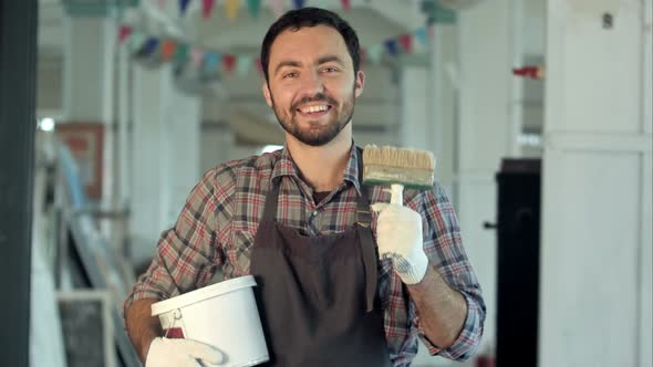 Happy Bearded Young Man Painter with Can Paint and Brush Standing and Smiling