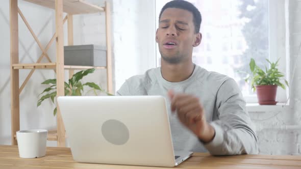 AfroAmerican Man Sitting in Office Upset By Loss Working on Laptop