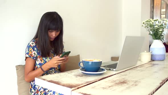 Attractive brunette asian girl sitting at the table in coffee shop with serious face and texting on